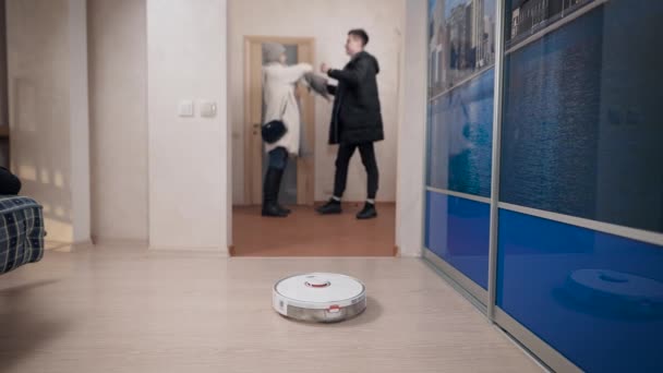Mladý pár jde na procházku, zatímco robot vysavač čistí. — Stock video