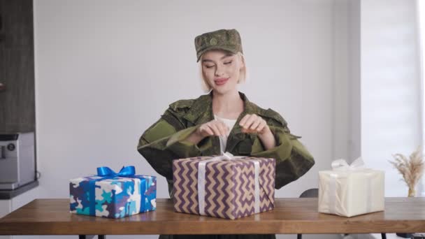 En blondin i militäruniform håller gåvor i sina händer. Överraskningen är inne i lådan. — Stockvideo
