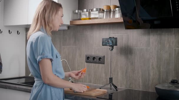 Egy háziasszony a konyhájában ételt készít és kommunikál az interneten. Egy nő videokapcsolaton keresztül beszél a barátjával.. — Stock videók