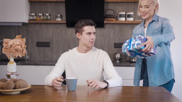 Jeune beau couple à la maison dans la cuisine. Une femme blonde offre à son mari un cadeau pour des vacances. — Video