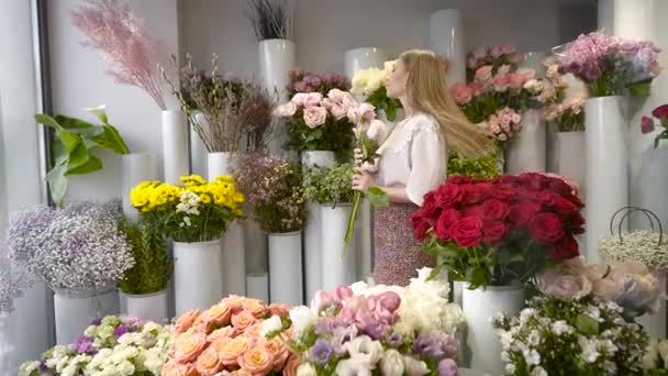 Una mujer en una florería recoge un ramo. Joven, en la nevera con una gran floristería de flores. — Vídeo de stock