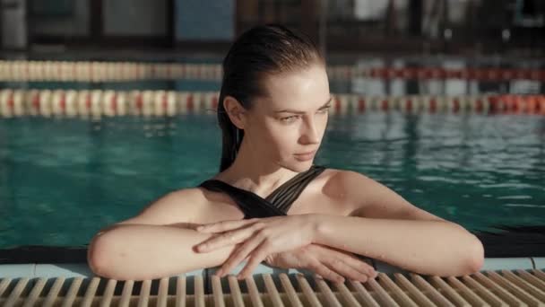 Retrato de uma mulher bonita contra o pano de fundo de uma grande piscina. Morena atraente em um maiô. — Vídeo de Stock