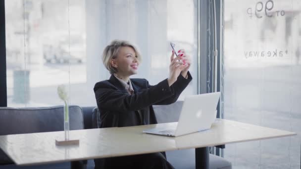 En blond kvinne på en kafe med telefon. Forretningskvinne tar en selfie. – stockvideo