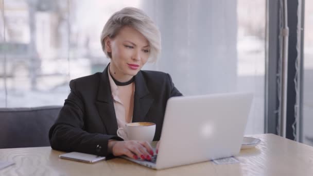 La donna lavora con un computer portatile in un caffè. Internet ti permette di fare affari da qualsiasi parte del mondo. — Video Stock
