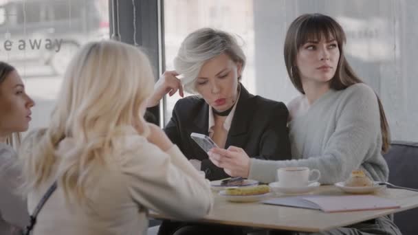 Four female friends in a modern cafe. Women enjoy drinks and sweets. — Stock Video