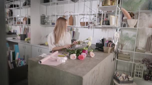 Uma florista mulher no local de trabalho coleta um arranjo de flores. — Vídeo de Stock