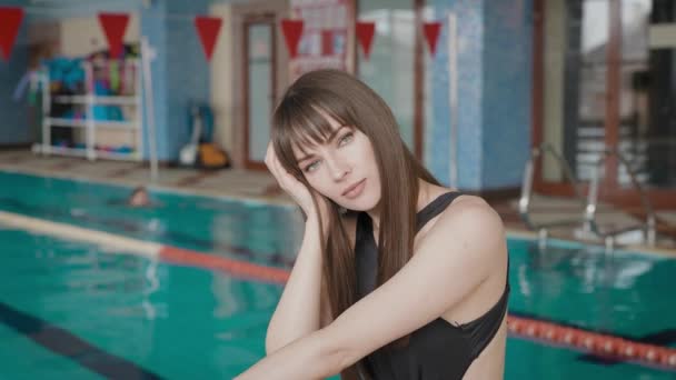 An attractive brunette is relaxing in the pool before exercising. Beautiful woman in a black swimsuit. — Stock Video