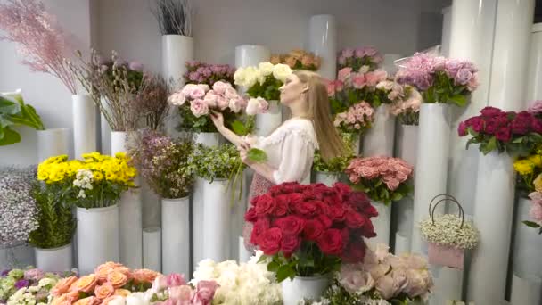 Uma mulher em uma loja de flores coleciona um buquê. Jovem, na geladeira com um grande florista de flores. — Vídeo de Stock