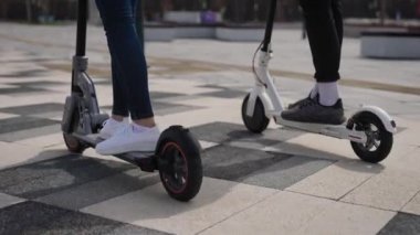 Bir erkek ve bir kadın elektrikli scooter kullanıyor. Çerçevede, scooterların bacakları ve ayaklıkları var..