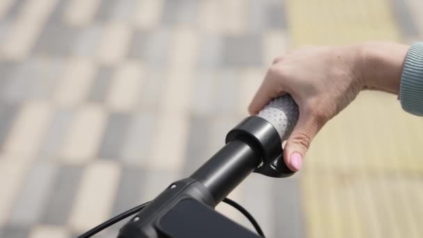 In het frame de handen van een jonge vrouw close-up. Een vrouw houdt haar elektrische scooter vast.. — Stockvideo