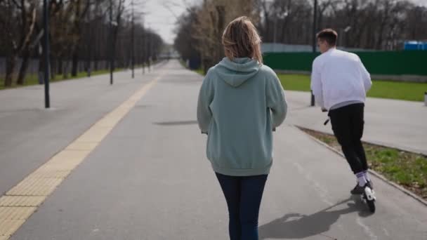 Una hermosa pareja de jóvenes monta en el parque en scooters eléctricos — Vídeos de Stock