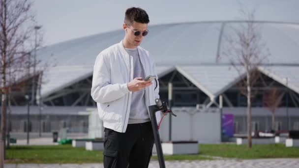 Un joven con un teléfono en las manos. Un hombre con auriculares inalámbricos blancos está teniendo una conversación. — Vídeo de stock