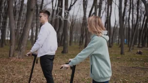 Ein schönes Paar junger Leute fährt mit Elektrorollern durch den Park — Stockvideo