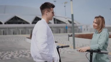 Genç bir adam ve kadın sokakta iletişim kuruyor. Çift gezintiye giderken elektrikli scooterları da yanlarında götürdü..