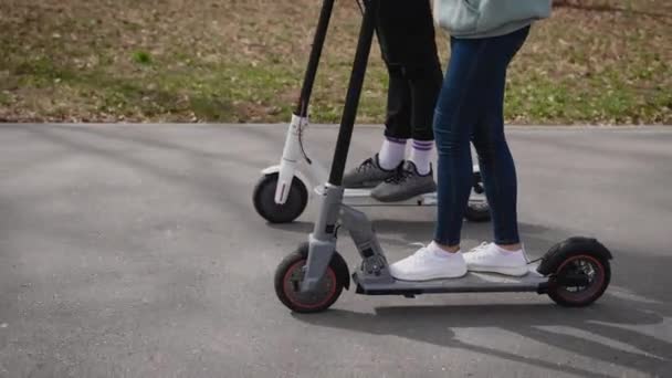 Un hombre y una mujer montan scooters eléctricos. En el bastidor, las patas y los pies de los scooters. — Vídeos de Stock