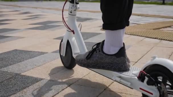 Pies de hombre en zapatillas de deporte en un scooter eléctrico. Transporte urbano eléctrico juvenil. — Vídeos de Stock