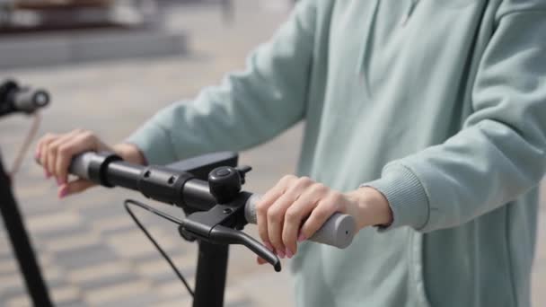 In het frame de handen van een jonge vrouw close-up. Een vrouw houdt haar elektrische scooter vast.. — Stockvideo