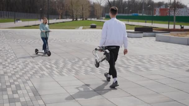 O homem está carregando uma scooter. A mulher está feliz em conhecer seu amigo. — Vídeo de Stock
