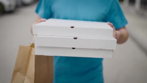 Un repartidor de comida irreconocible lleva cajas de pizza y bolsas de comida. — Vídeo de stock