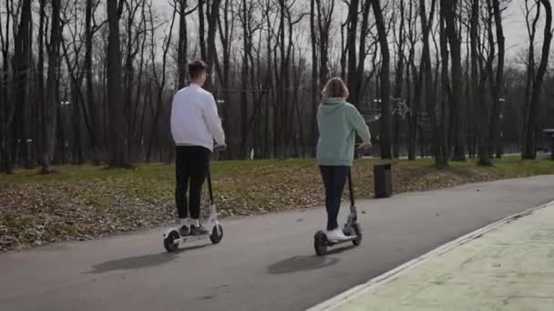 Ein schönes Paar junger Leute fährt mit Elektrorollern durch den Park — Stockvideo