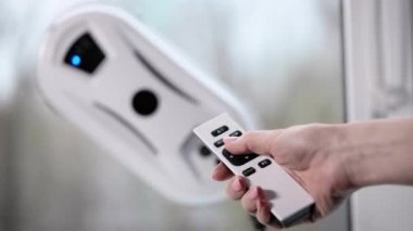 Bir kadın bir robotu kontrol ediyor. Kontrol paneli pencere temizleme programını başlatmak için kullanılabilir.