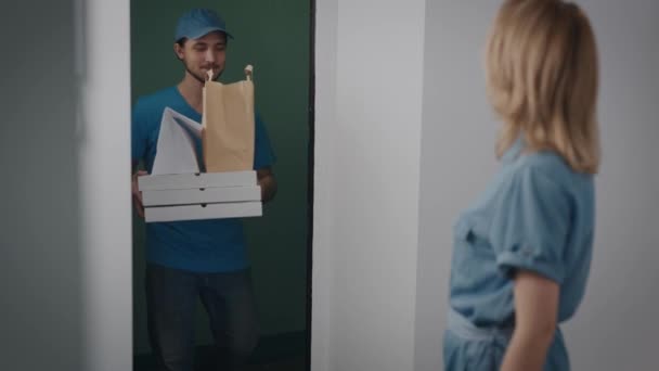 El repartidor trajo un pedido con comida. Un hombre con uniforme azul, amable y guapo. El ama de casa acepta la orden del mensajero. — Vídeos de Stock