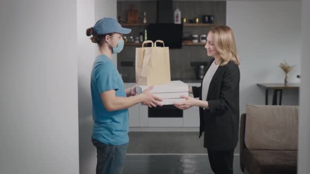 Un joven repartidor trajo pizza y otra comida a casa. Mujer de negocios toma un pedido en su apartamento. — Vídeo de stock