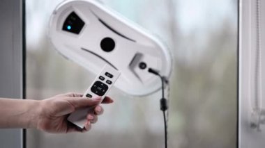 Bir kadın bir robotu kontrol ediyor. Kontrol paneli pencere temizleme programını başlatmak için kullanılabilir.