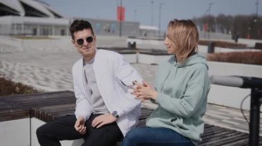 Bir adam ve bir kadın bankta oturmuş sohbet ediyorlar. Çiftin yanında elektrikli scooterları var..