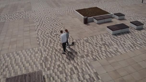 Luchtfoto 's. Een man en een vrouw staan te praten. Jongeren bereden hun elektrische scooters. — Stockvideo