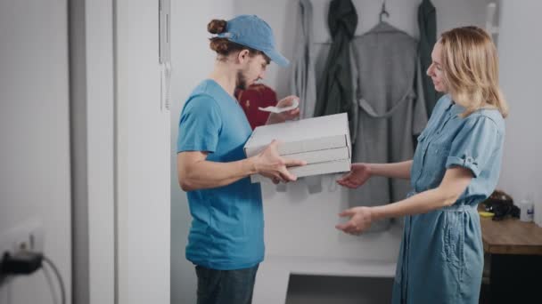 Un joven repartidor de comida con uniforme azul. Un hombre trajo pizza y una bolsa de comida a una hermosa mujer.. — Vídeos de Stock