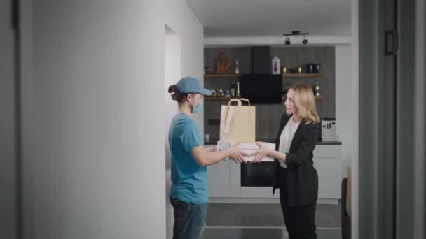 Un joven repartidor trajo pizza y otra comida a casa. Mujer de negocios toma un pedido en su apartamento. — Vídeos de Stock