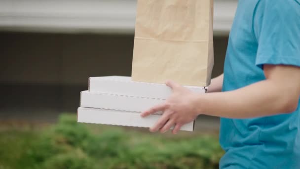 Un repartidor de comida irreconocible lleva cajas de pizza y bolsas de comida. — Vídeo de stock