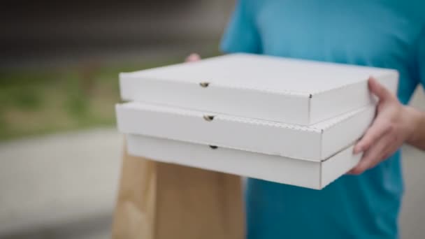 Un repartidor de comida irreconocible lleva cajas de pizza y bolsas de comida. — Vídeo de stock