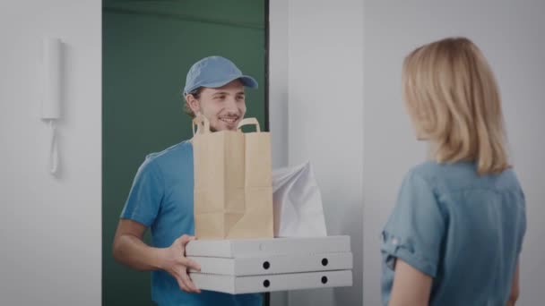 El repartidor trajo un pedido con comida. Un hombre con uniforme azul, amable y guapo. El ama de casa acepta la orden del mensajero. — Vídeos de Stock