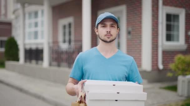 Na ulici stojí atraktivní poslíček s objednávkou. Muž v modrém tričku a čepici pracuje.. — Stock video