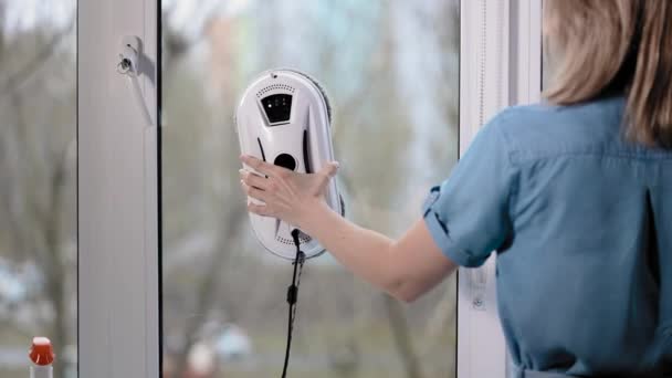 Una hermosa ama de casa instala un robot más limpio. El limpiador robot funciona en modo automático y se arrastra en ventanas y espejos. — Vídeos de Stock