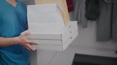 Yemek dağıtan bir adam siparişi bir kadına verir. Pizza kutularına ve yemek paketlerine yakın çekim.