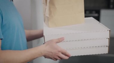 Yemek dağıtan bir adam siparişi bir kadına verir. Pizza kutularına ve yemek paketlerine yakın çekim.