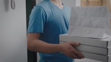 Teslimatçı elinde yemekle bir sipariş tutuyor. Yarı zamanlı bir işte çalışan bir gencin portresi..