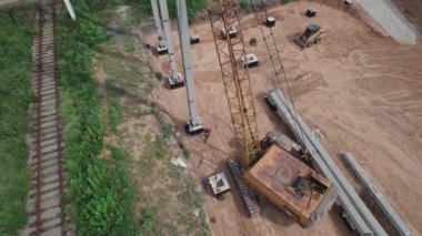 Hava görüntüsü. İşçiler beton direkler kurmak için büyük bir vinç kullanıyorlar. İnşaat