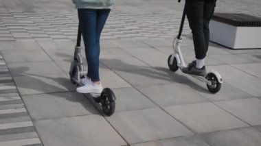 Bir erkek ve bir kadın elektrikli scooter kullanıyor. Çerçevede, scooterların bacakları ve ayaklıkları var..
