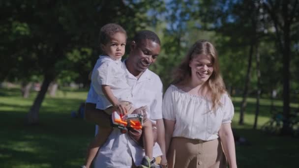 Μια πολυεθνική οικογένεια περπατάει στο πάρκο. Αφρο-Αμερικανός πατέρας με τη γυναίκα και το παιδί του. — Αρχείο Βίντεο