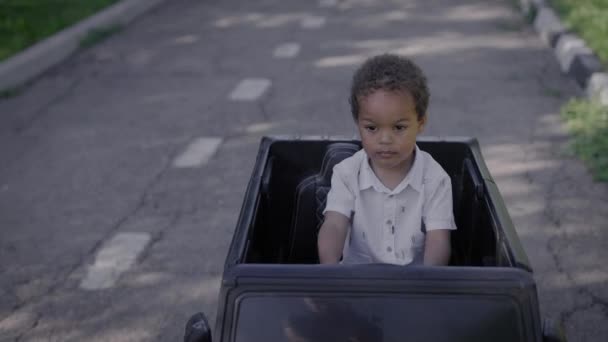 Söt afroamerikansk pojke i en leksaksbil. Pojke och åk i parken. — Stockvideo