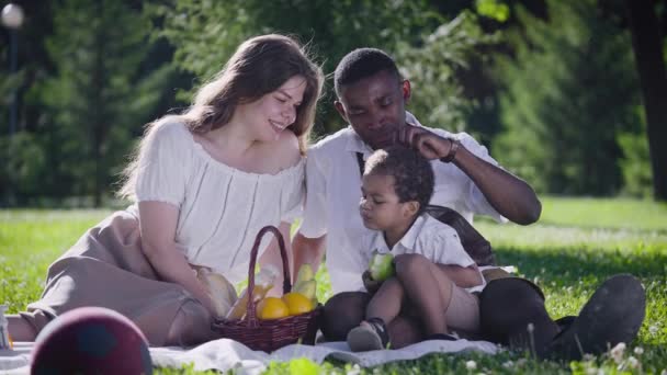 A cute multicultural family had a picnic in the park. Mom, dad and son sat on a blanket, next to a basket of food. — Stock Video