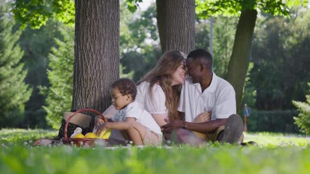 A cute multicultural family had a picnic in the park. Mom, dad and son sat on a blanket, next to a basket of food. — Stock Video