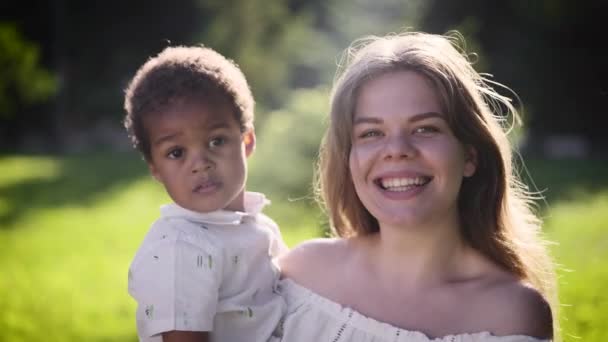 Feliz mujer europea de piel clara sostiene a la niña africana en sus brazos. — Vídeo de stock