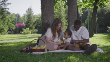 Siyah baba, açık tenli anne ve parkta mestizo çocuk. Parkta piknik yapan mutlu bir aile. Neşeli
