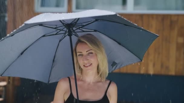 Atractiva rubia bajo la lluvia de verano. Una mujer bonita usa un paraguas para protegerse de una tormenta. — Vídeos de Stock