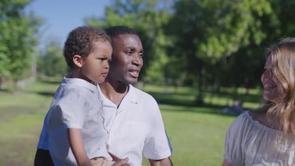 W parku spaceruje wielonarodowa rodzina. Afroamerykanin ojciec z żoną i dzieckiem. — Wideo stockowe